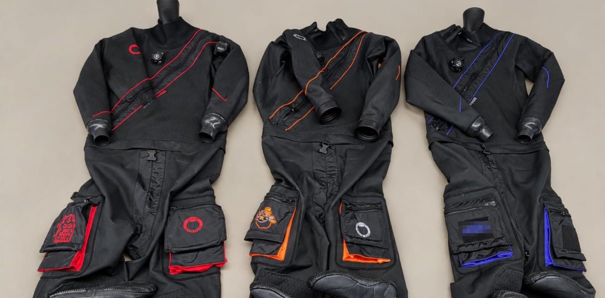 Drei schwarze Hauberk Drysuits mit roten, orangen und blauen Akzenten